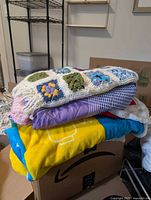 Stack of three blankets showing crocheted afghan, geometric picnic blanket, LEGO fleece throw