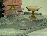 Group shot of all six pressed glass serving pieces arranged on table, including pedestal stand, platters, bowls, amber compote
