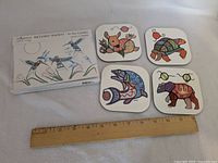 Overall view of boxed greeting cards, four coasters and ruler for scale