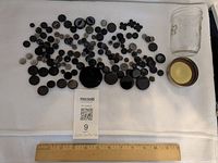 Overview of buttons spread on cloth beside jar and ruler for scale