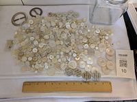 Overview of buttons spread out, buckles, jar and ruler for scale