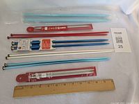 Overview of six pairs of knitting needles assorted colors and lengths with ruler for scale
