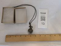 Pendant watch on chain beside box and ruler for scale
