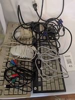 Two keyboards (beige Compaq, black generic) stacked with two white Nexxtech mice, VGA cable, power cord and assorted cables visible