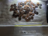 Mixed pile of US pennies on white cloth beside labelled bag
