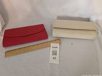 Red fabric clutch and off-white clutch with ruler showing scale