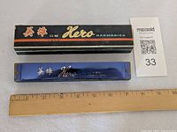 Top view of harmonica beside branded box and ruler