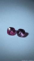 Two vibrant pink cushion-cut spinels on neutral background