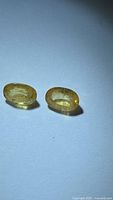 Two oval yellow sapphires on white background under diffused light