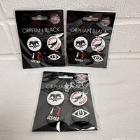 Three sealed Orphan Black pin packs on display
