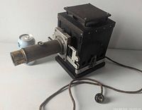 Front and side view of metal slide projector with brass lens and cord for scale