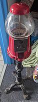 Full view of gumball machine showing red body, glass globe, coin mechanism, black cast iron stand