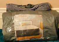 Rolled grey air mattress with taped product sheet front view showing Dura-Beam Deluxe queen model