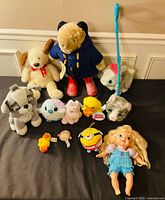 Group shot of all 12 stuffed toys and doll on black surface