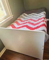 Side view of assembled twin bed with bedding, showing white frame