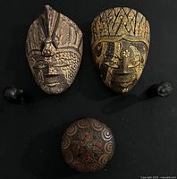 Two carved and painted wooden masks, two small dark carvings and round carved box displayed on black background