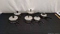 Six stainless steel saucepans with matching lids displayed on table