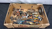 Top view of cardboard box showing assorted hand tools including pliers, grinding discs and torch head