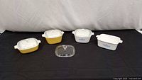 Four Corning Ware dishes with lids and extra lid displayed