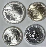 Four silver coins in capsules, showing Olympic designs, sailboats, world map, and Maple Leaf