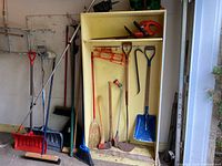 Full view of cabinet with assorted shovels, brooms, hedge trimmer, cord hangers and spreaders