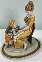 Full view of figurine showing woman reading and boy leaning with hat