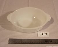 Top view of oval milk glass casserole dish next to ruler