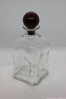 Front view of clear square glass decanter with red ball stopper fitted