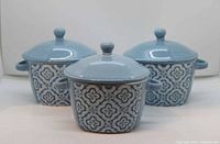 Front view of three blue stoneware handled bowls with patterned sides and lids