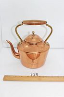 Front view of polished copper kettle with lid, spout, wood handle, ruler for scale