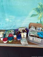 Overall lot on tabletop showing candles, floral supplies, bead containers, pinecones, foam items