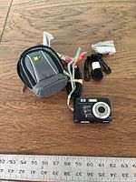 Group shot of camera, case, cable, straps with ruler for scale