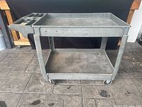 Front view of grey two-shelf Rubbermaid cart with side organizer and casters