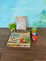 Full lot showing Munchkin Deluxe, Munchkin Zombies, Apples to Apples dice container, Uno dice tin, green frog plush