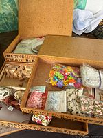 Open cork box showing wood cubes, packets of beads and embellishments