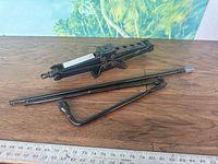 Scissor jack, jack arm lug wrench displayed on wood surface with ruler for scale