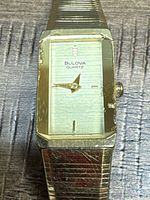 Close-up of watch face showing Bulova Quartz branding, rectangular gold-tone case, wear and scratches