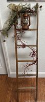 Full view of decorated wooden ladder with lantern and greenery