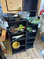 Overall lot view on shelving showing Bundt pans, ceramic dishes, Pyrex bowl, utensils