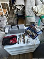 Closed grey Dremel case, red-black tool pouch, wrenches and brushes on white surface