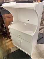 Front view of white melamine kitchen cart cabinet showing top, open shelf, drawer, doors, cord hole