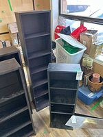 Black and brown laminate shelving units standing on floor, showing relative heights and open shelves