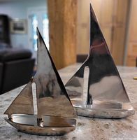 Both polished aluminum sailboat sculptures showing scale difference