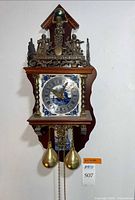 Front view of Dutch wall clock showing ceramic dial surround, brass crest, weights and chains