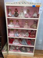 Full view of white wood display cabinet with floral trim and dolls on four shelves