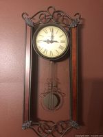 Front view of clock showing face, pendulum, metal scroll frame and wood columns