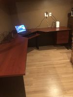 Overall view of L-shaped desk with chair area, showing laminate surface and keyboard tray.
