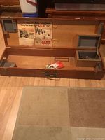 open wooden box showing interior compartments, flyer, envelope, metal component