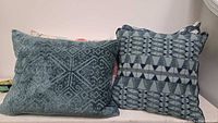 Front view of dark aqua Aztec pattern cushion beside navy/teal triangle pattern cushion