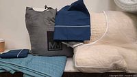 All items grouped: mattress cover in grey bag, teal shams, navy pillowcases, cream coverlet